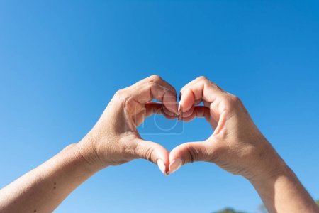 womans hands showing heart sign on blue sky background,