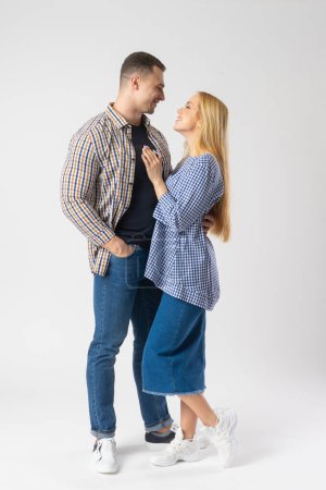 Foto de El hombre y la mujer se abrazan mirándose. Pareja joven casada con ropa casual. Modelos posando sobre fondo blanco - Imagen libre de derechos