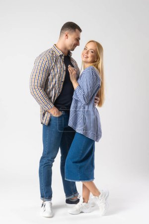 Foto de Hombre y mujer abrazándose mientras miran a la cámara. Pareja joven casada con ropa casual. Modelos posando sobre fondo blanco - Imagen libre de derechos