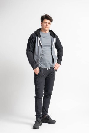Foto de Joven hombre moreno en chándal negro, camiseta gris y zapatillas de running posando en el estudio sobre fondo blanco - Imagen libre de derechos