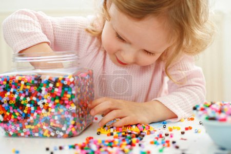Téléchargez les photos : Ttle Girl Engrossed en jouant avec des perles colorées - en image libre de droit