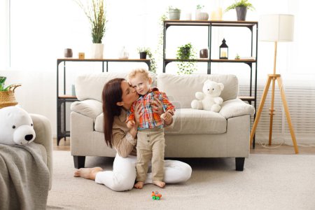 Foto de Feliz familia madre y pequeño bebé juega con el hijo en la sala de estar. - Imagen libre de derechos