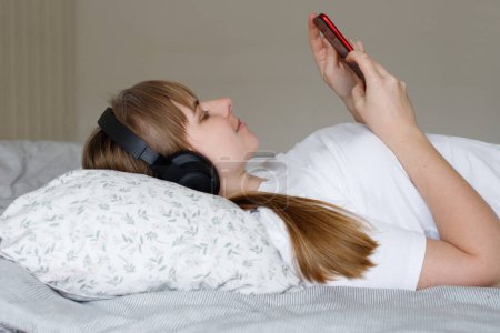 mujer en auriculares escuchando música con smartphone en la cama en casa