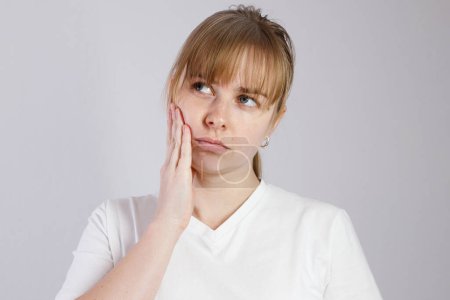 mujer 30s tiene un dolor de muelas, sosteniendo su mejilla