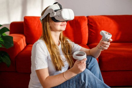 Téléchargez les photos : Femme excitée portant réalité virtuelle VR lunettes casque dans le salon. Tendance future en utilisant un appareil de lunettes de réalité virtuelle pour le jeu vidéo et le divertissement à domicile. Expérience technologique futuriste. - en image libre de droit