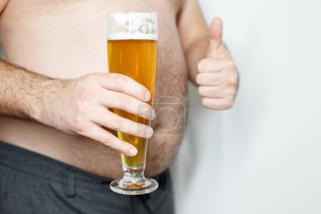close-up of a man with a beer belly suffering from excess weight with a glass of beer