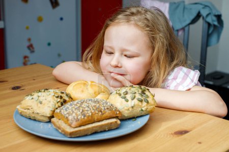 Photo for Nutrition and food for the child. the girl is interested in the bread on the table. - Royalty Free Image