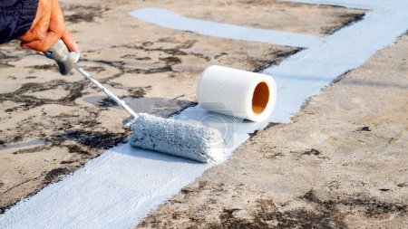Téléchargez les photos : Revêtement de sol gris peint à la main avec rouleau de peinture pour filet imperméable et renforcé. Réparation plancher de pont imperméabilisation. - en image libre de droit