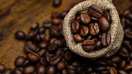 Photo for Roasted coffee beans placed on sack, wooden background - Royalty Free Image