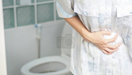 Téléchargez les photos : Femme se tenait dans la salle de bain dans les toilettes. Avec diarrhée sévère Utilisez les deux mains pour maintenir l'estomac, douleur, torsion, torture. - en image libre de droit