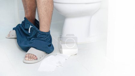 Téléchargez les photos : Diarrhée. Homme assis près de la cuvette des toilettes sur un fond blanc. - en image libre de droit