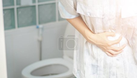 Téléchargez les photos : Femme se tenait dans la salle de bain dans les toilettes. Avec diarrhée sévère Utilisez les deux mains pour maintenir l'estomac, douleur, torsion, torture. - en image libre de droit