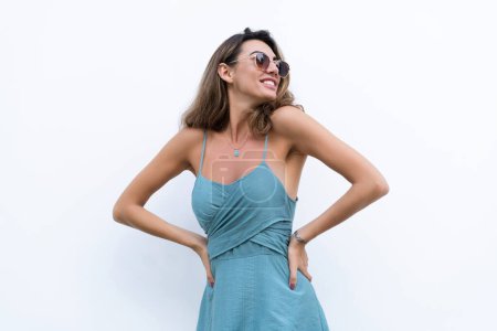 Téléchargez les photos : Portrait de belle femme en robe d'été ajustée verte sur fond blanc lumière naturelle du jour, portant des lunettes de soleil, souriant excité - en image libre de droit