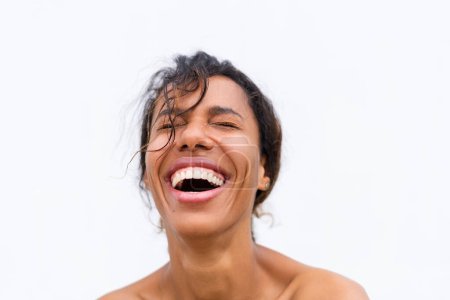 Téléchargez les photos : Portrait de beauté de jeune femme afro-américaine nue aux épaules nues sur fond blanc avec une peau parfaite et un maquillage naturel positif rire - en image libre de droit