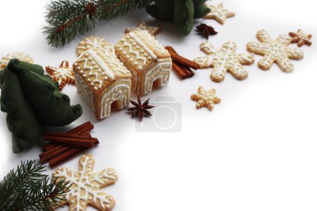 Foto de Pequeñas casas de pan de jengibre con muchas galletas de jengibre en forma de estrellas y copo de nieve en blanco con ramas de pino, canela y especias de anís estrellado en enfoque selectivo - Imagen libre de derechos