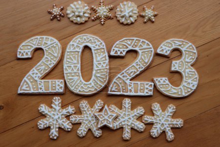 Gingerbread cookies with sugar glaze decoration in the form of numbers 2023 on wooden background. Many Gingerbread cookies in star and snowflake shape. New year concept