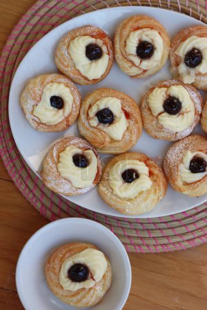 Foto de Italian traditional fried Zeppole for St. Joseph (Fathers day). Homemade sweet pastry with custard cream and black cherries on white plate on wooden table - Imagen libre de derechos