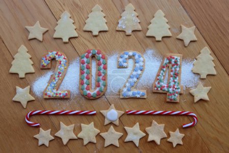 Foto de Galletas de corteza corta con espolvoreos de colores en forma de números 2024 con bastones de caramelo en la mesa de madera - Imagen libre de derechos