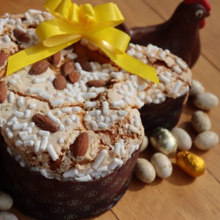 Colomba Pasquale. Sweet Easter cake with dark chocolate hen and eggs wrapped in foil. Italian traditional pastry on wooden table