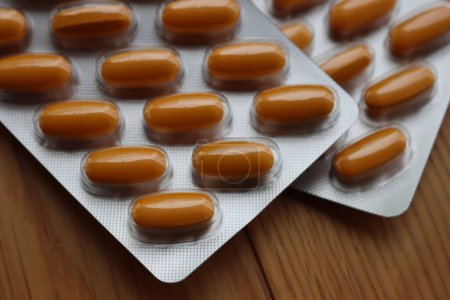 Pharmaceutical medicine capsules on wooden table. Orange pills in blister packaging