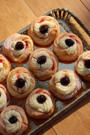 Italian traditional fried Zeppole on a golden cardboard tray for St. Joseph (Fathers day). Homemade sweet pastry with custard cream and black cherries in syrup