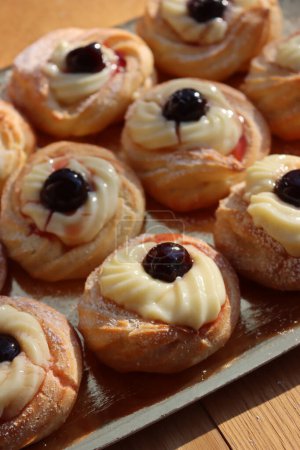 Italian traditional fried Zeppole on a golden cardboard tray for St. Joseph (Fathers day). Homemade sweet pastry with custard cream and black cherries in syrup