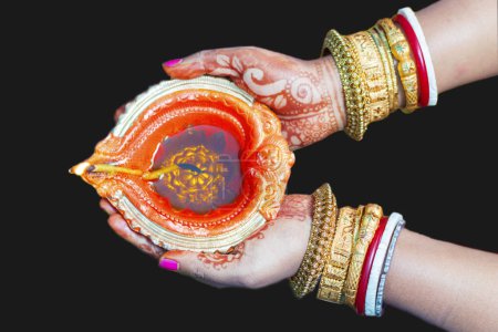 Selektive Fokussierung einer schönen Dame, die goldene Armreifen trägt, mit Händen, die Kerzen beleuchtete Diya halten.