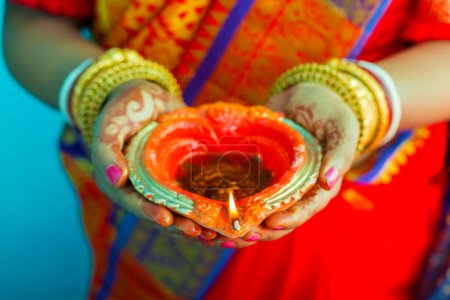 Selektive Fokussierung einer schönen Dame, die goldene Armreifen trägt, mit Händen, die Kerzen beleuchtete Diya halten.