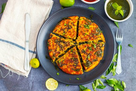 selective focus of Gujrati dish handvo slice tringle cut decorated with lemon, curry leaves, mint chutney and tomato sauce.