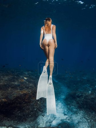 Photo for Behind view of woman freediver with white fins underwater. Freediving with beautiful girl in deep ocean - Royalty Free Image