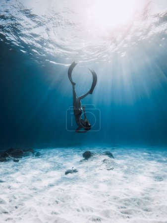 Téléchargez les photos : Femme plongeur avec nageoires plonger au fond de la mer. Plongée libre dans l'océan bleu avec les rayons du soleil - en image libre de droit