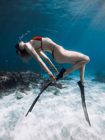 Téléchargez les photos : Femme en bikini avec corps sexy posant sous l'eau sur fond sablonneux dans un océan bleu transparent. - en image libre de droit