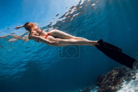 Photo for Sexy woman in bikini with fins glides underwater. Woman with beautiful figure posing in blue ocean - Royalty Free Image