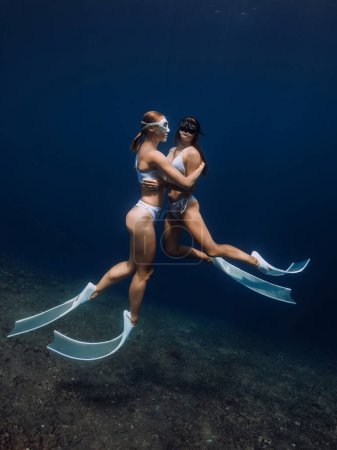Photo for Woman freedivers hugging and glides in deep ocean. Freediving with couple girls in underwater - Royalty Free Image
