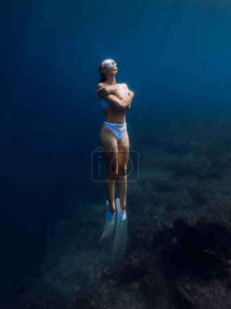 Téléchargez les photos : Femme plongeuse libre en bikini blanc avec des nageoires blanches glisse sous l'eau dans l'océan bleu tropical - en image libre de droit