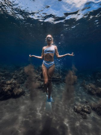 Foto de Mujer freediver en bikini blanco con arena en las manos se desliza bajo el agua en el océano azul - Imagen libre de derechos