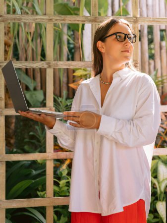 Téléchargez les photos : Jeune fille positive avec ordinateur portable posant en co travailler avec la lumière du soleil - en image libre de droit