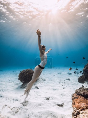Téléchargez les photos : Freediver lady glides underwater near coral reef with tropical fish and sunset or sunrise sunlight in blue ocean - en image libre de droit