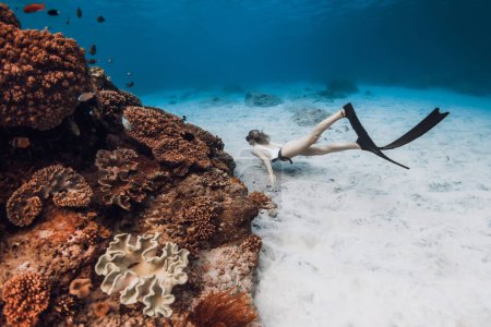 Téléchargez les photos : Freediver woman in bikini swim with fins near coral reef in blue ocean - en image libre de droit