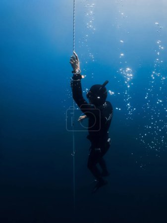 Foto de October 03, 2022. Amed, Indonesia. Professional freediving underwater in transparent sea. Men in wetsuit with fins training on deep in blue ocean. - Imagen libre de derechos