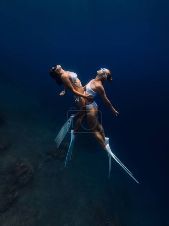 Photo for Couple of girls freedivers hugging and posing in deep ocean. Freediving with couple woman in underwater - Royalty Free Image