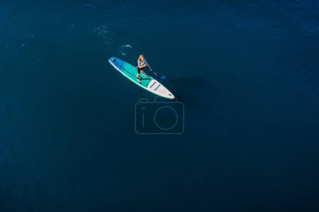 Téléchargez les photos : Young girl rowing on stand up paddle board at quiet sea. Woman on SUP board in blue sea. Aerial view - en image libre de droit