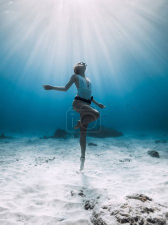 Téléchargez les photos : Un plongeur posant sous l'eau. Plongée libre avec femme dans l'océan bleu avec fond sablonneux et rayons du soleil - en image libre de droit