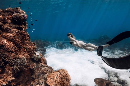 Téléchargez les photos : Slim woman in bikini swim with fins near coral reef in blue ocean. Freediving with beautiful girl - en image libre de droit