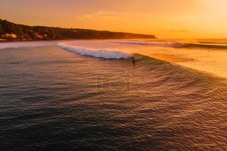 Photo for Aerial view of surfing waves at warm sunset. Perfect swell and surfer ride on wave in Bali - Royalty Free Image
