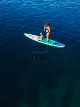 Foto de 24 de julio de 2022. Antalya, Turquía. Mujer delgada con niño remando en stand up paddle board en el mar tranquilo. Mujer con hija pequeña en Red Paddle SUP bordo en el mar. - Imagen libre de derechos