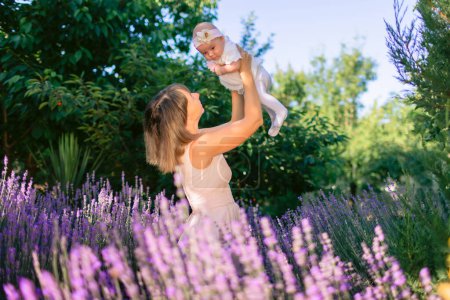 Téléchargez les photos : Mère heureuse jouer avec sa fille bébé en plein air avec des fleurs de lavande fleur - en image libre de droit