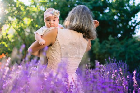 Foto de Madre con su bebé en el jardín con flores de lavanda y sol - Imagen libre de derechos