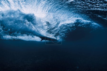 Wave underwater and surfer ride on surfboard in ocean. Underwater crashing wave and surfboard in transparent water