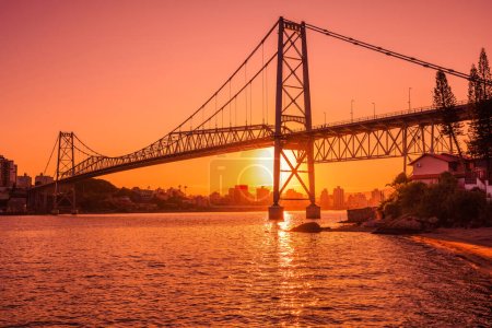 Puente antiguo Hercilio luz con cálida puesta de sol y reflexión sobre el agua en Florianópolis
